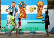 Indian boys play football on street in front of wall painted...