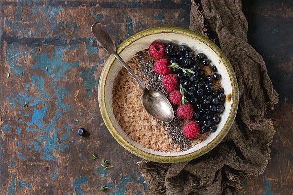 Bowl of oatmeal porridge with blueberries, raspberries and chia seeds, served with sackcloth rag and vintage spoon over old wood textured background. Rustic breakfast theme. Top view, space for text