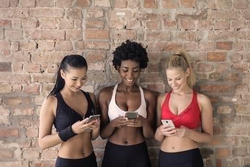 Three Woman in Assorted-color Sport Bras Holding and Watching Their Smartphones