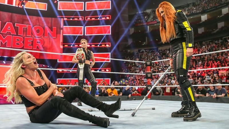 Becky Lynch attacking Charlotte Flair while Ronda Rousey looks on