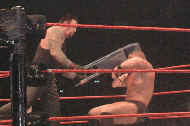 The Undertaker dishes out a chair shot to the head.