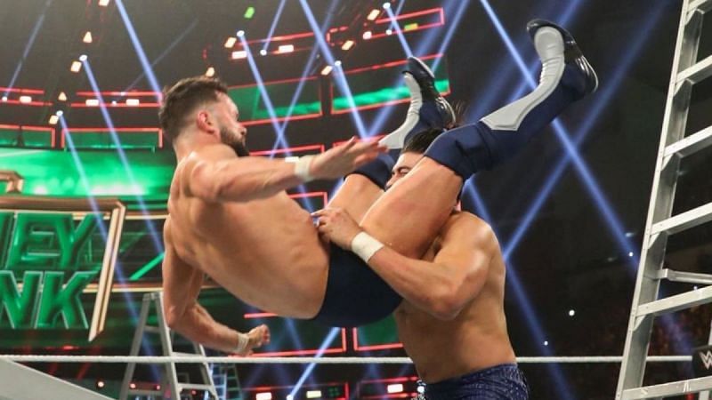 Andrade powerbombs Finn Balor onto the ladder.