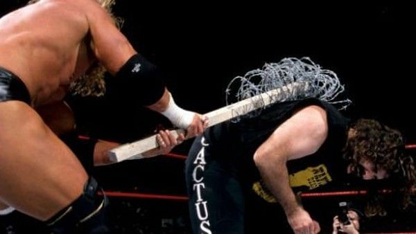 Triple H hits Mick Foley with a barbed wire wrapped board.