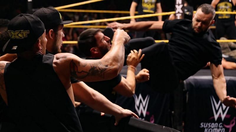 Finn Balor driving Johnny Gargano through the barricade with a front dropkick.