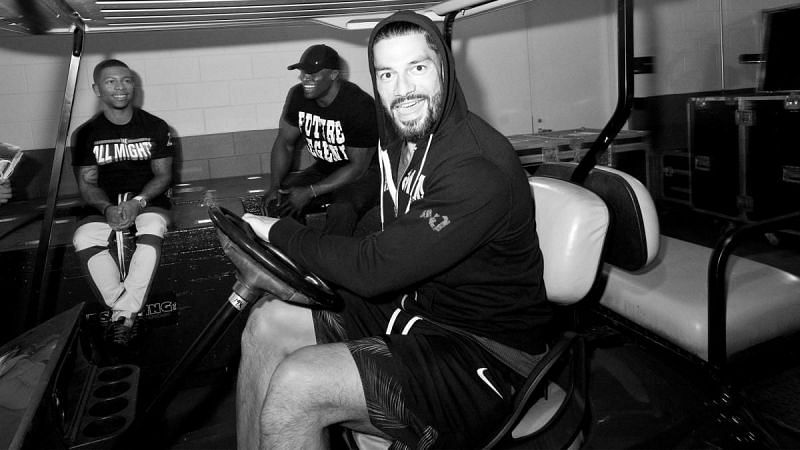 Roman Reigns driving a cart, as Lashley and Rush look on.