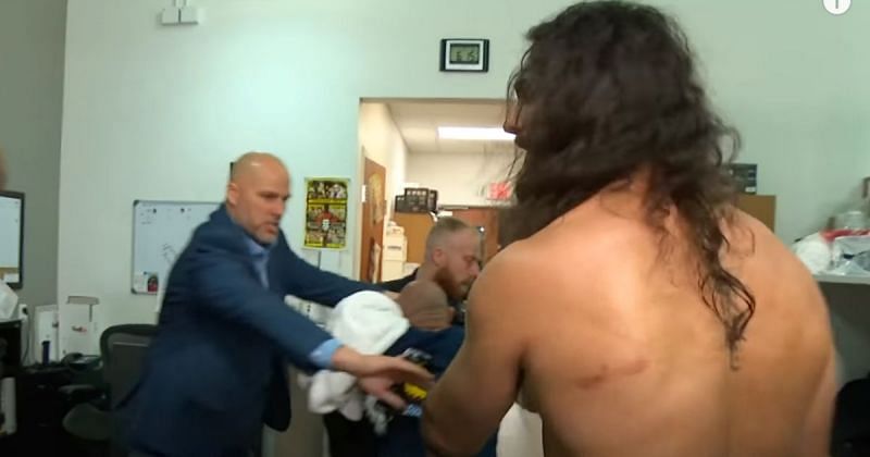 Rey Mysterio gets escorted by WWE officials backstage as Seth Rollins tries to talk to him.