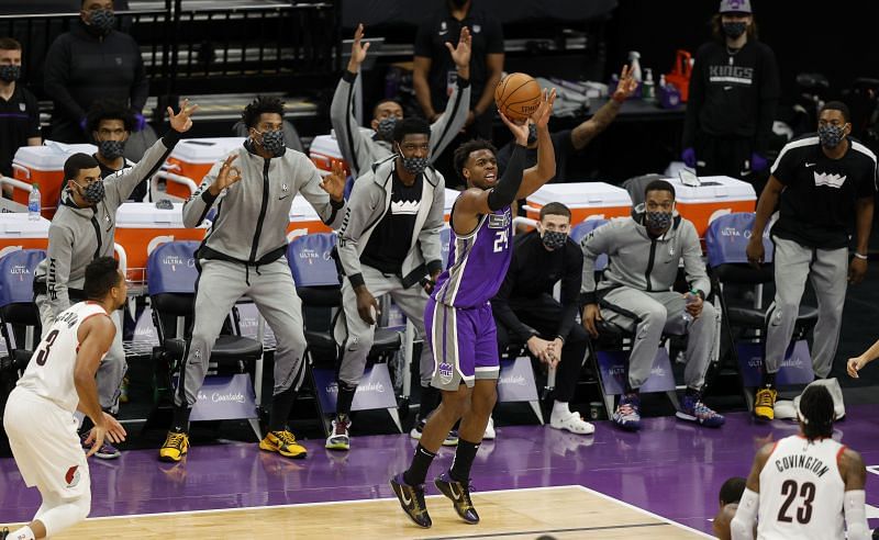 Buddy Hield of the Sacramento Kings attempts a three in front of teammates on the bench, who are all wearing masks, during the first period of their game against the Portland Trail Blazers