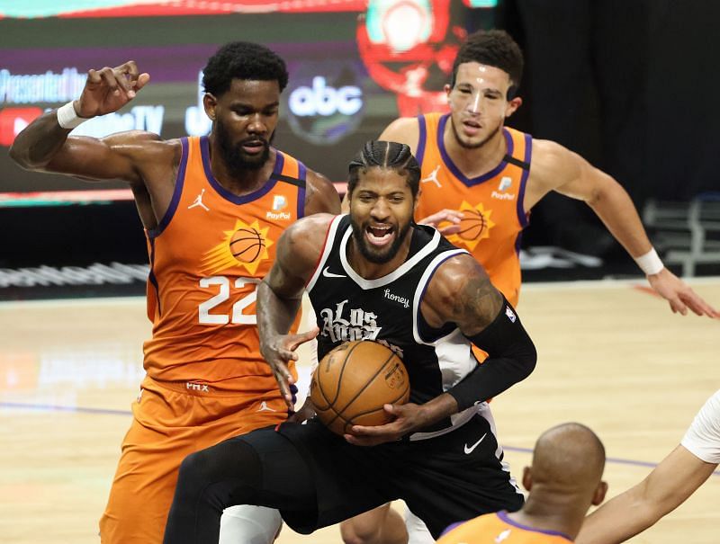 Paul George #13 drives between Deandre Ayton #22 and Devin Booker #1.