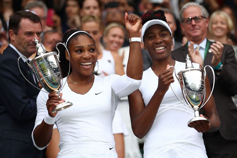 Venus Williams and Serena Williams hold up the ladies doubles trophies at Wimbledon in 2016