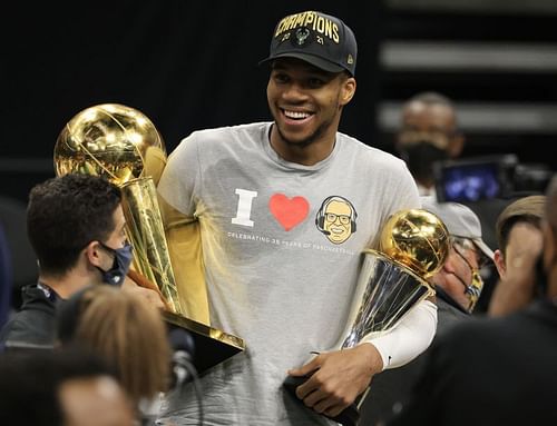 Giannis Antetokounmpo #34 holds the Bill Russell NBA Finals MVP Award and the Larry O'Brien Championship Trophy.