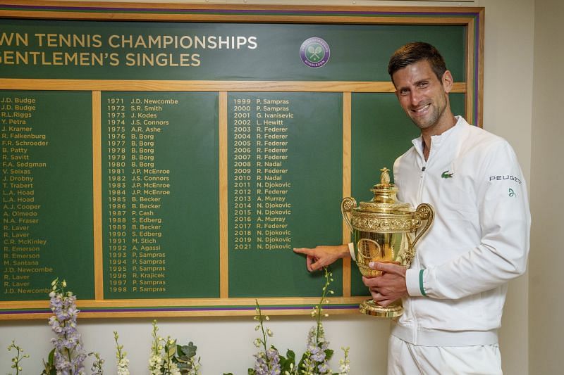 Novak Djokovic poses with his title beside the Wimbledon winners board