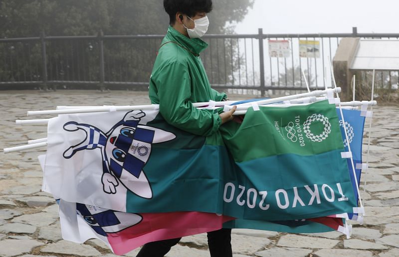 A staff wearing a protective face mask, amid the coronavirus disease (COVID-19) pandemic, carries flags after an unveiling ceremony of Olympic symbol