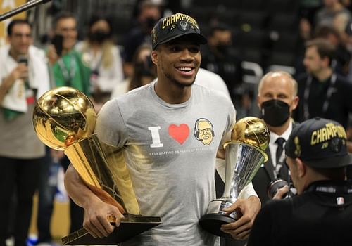 Giannis Antetokounmpo #34 holds the Bill Russell NBA Finals MVP Award and the Larry O'Brien Championship Trophy.