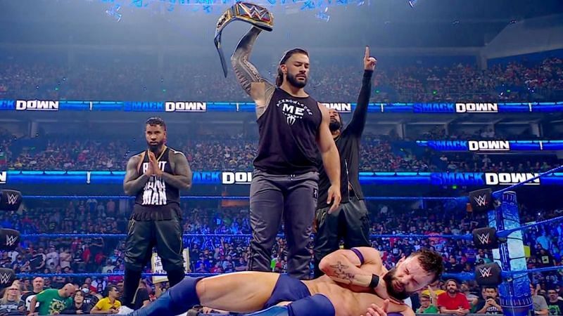 WWE सुपरस्टार फिन बैलर पर अटैक के बाद अपनी यूनिवर्सल चैंपियनशिप को दिखाते चैंपियन रोमन रेंस जबकि साथ हैं द उसोज़