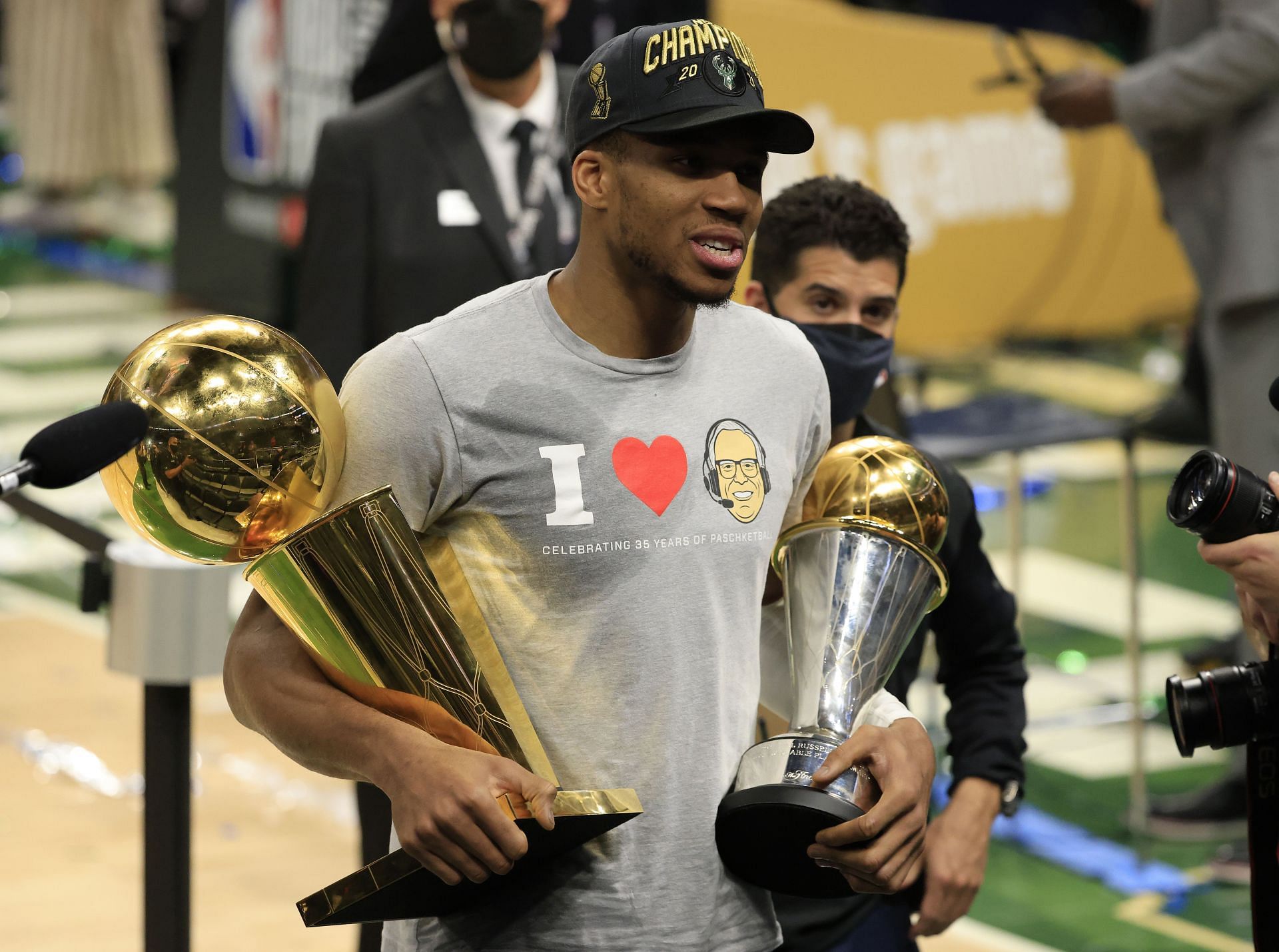 Giannis Antetokounmpo holding the Larry O'Brien trophy and NBA Finals trophy.