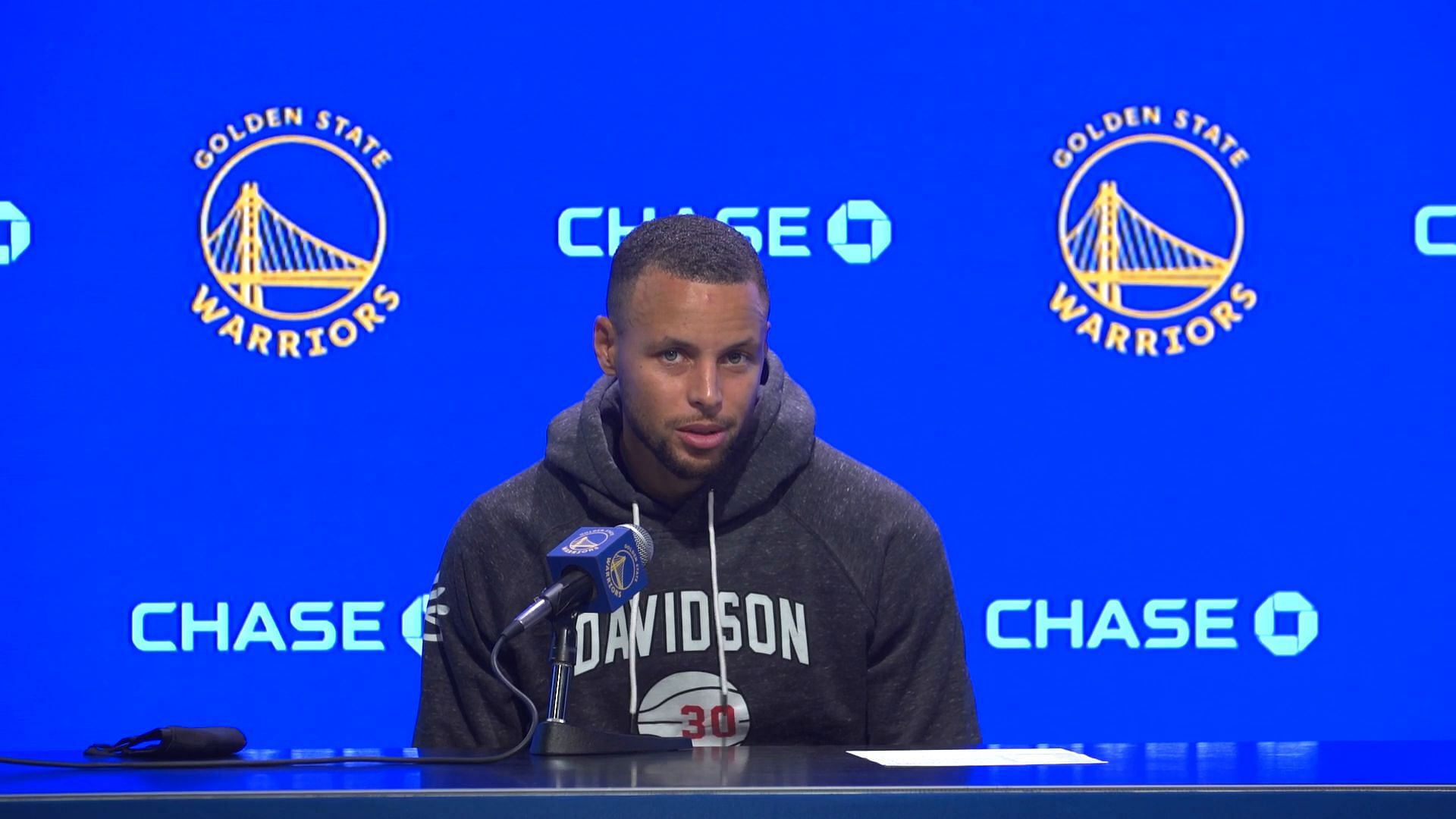 Stephen Curry speaking at a postgame press conference with Chase in the backdrop.