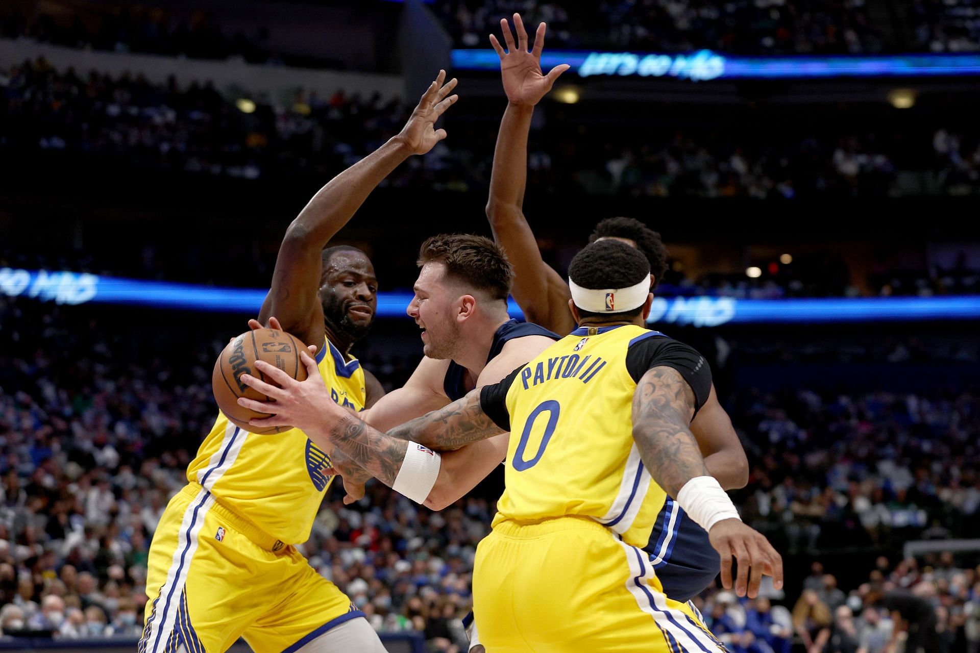 Luka Doncic of the Dallas Mavericks draws a foul against Draymond Green, left, of the Golden State Warriors and Gary Payton II in the first quarter at American Airlines Center on Wednesday in Dallas, Texas.