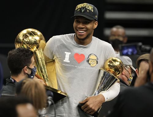 Giannis Antetokounmpo #34 of the Milwaukee Bucks holds the Bill Russell NBA Finals MVP Award and the Larry O'Brien Championship Trophy.