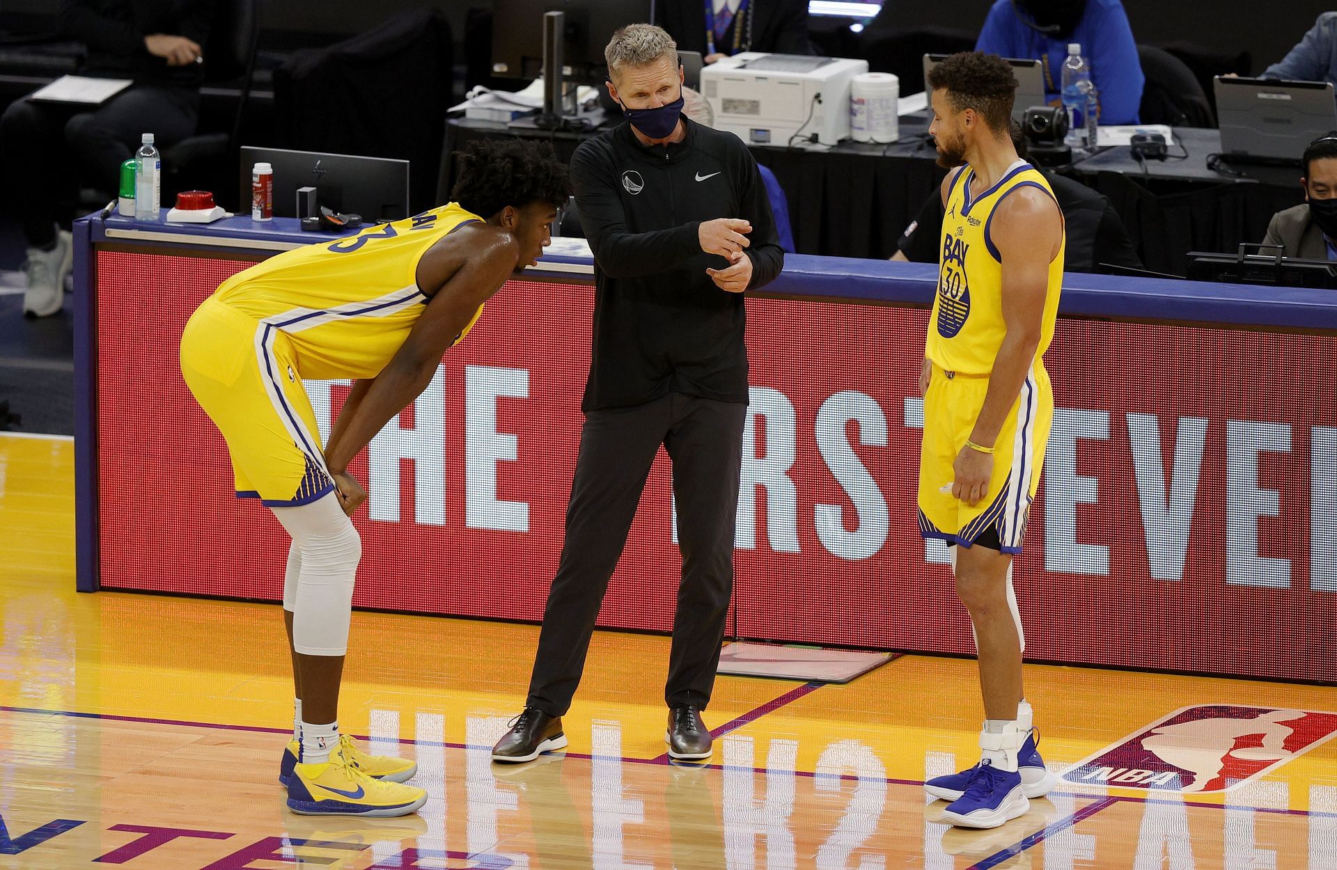 James Wiseman and Steph Curry talk to coach Steve Kerr during a timeout.