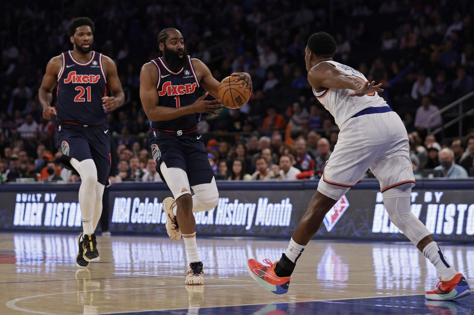 James Harden of the Philadelphia 76ers passes the ball back to Joel Embiid (21) in front of RJ Barrett of the New York Knicks during the first half on Sunday in New York City.