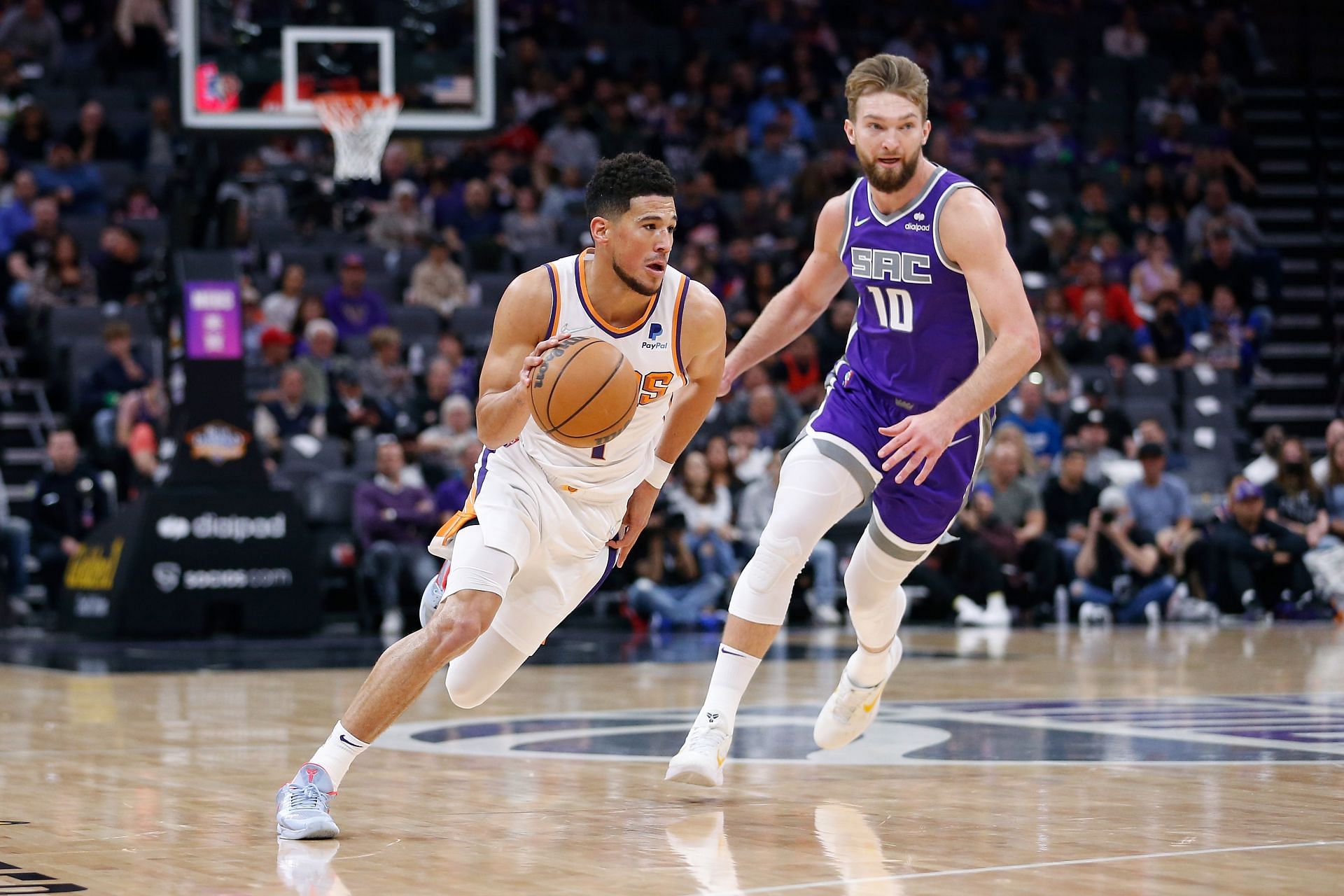 Devin Booker #1 of the Phoenix Suns dribbles the ball up court against Domantas Sabonis #10 of the Sacramento Kings in the first quarter at Golden 1 Center on March 20, 2022 in Sacramento, California.