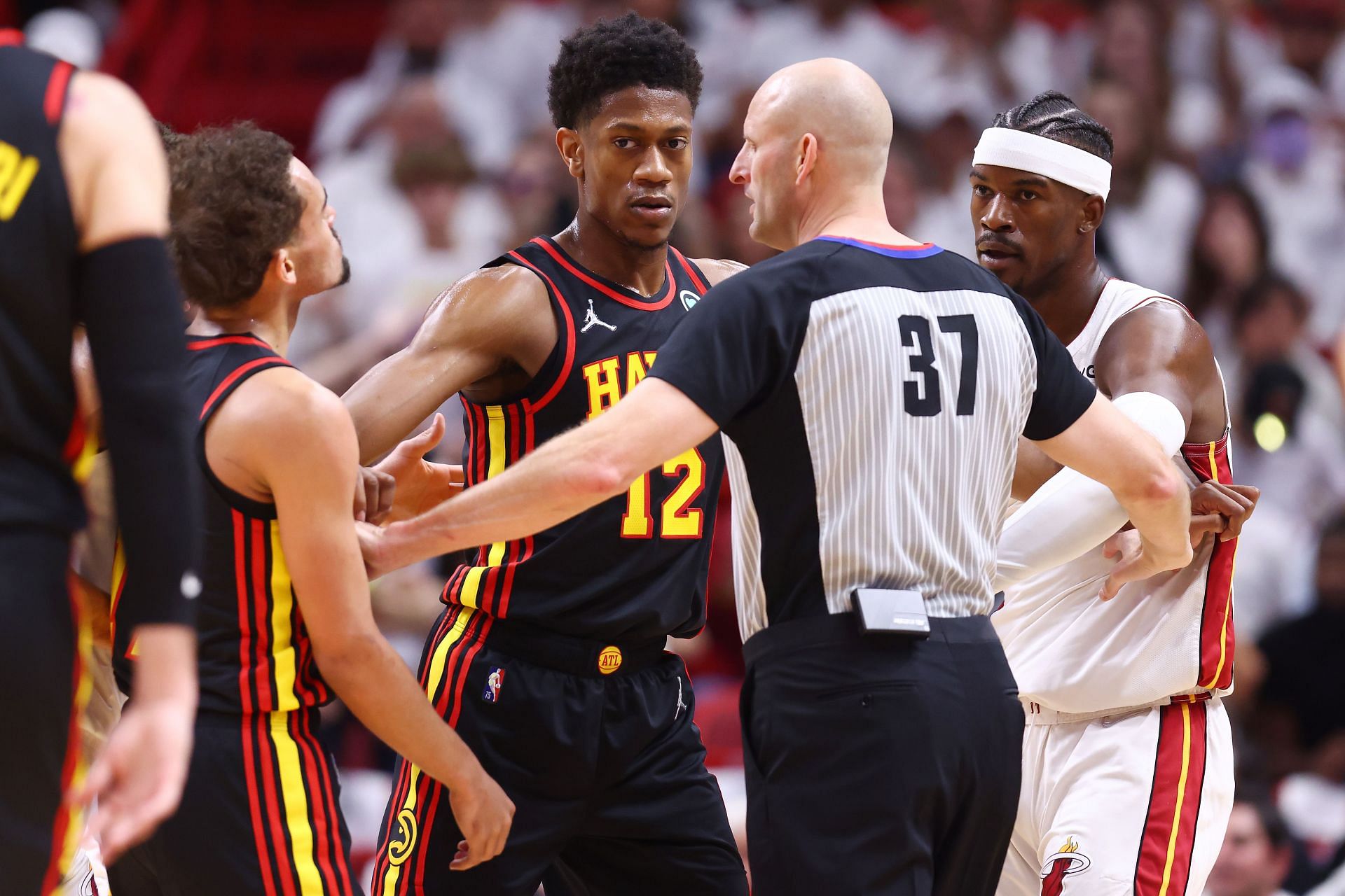 Trae Young of the Atlanta Hawks and Jimmy Butler of the Miami Heat are separated by referee Eric Dalen.