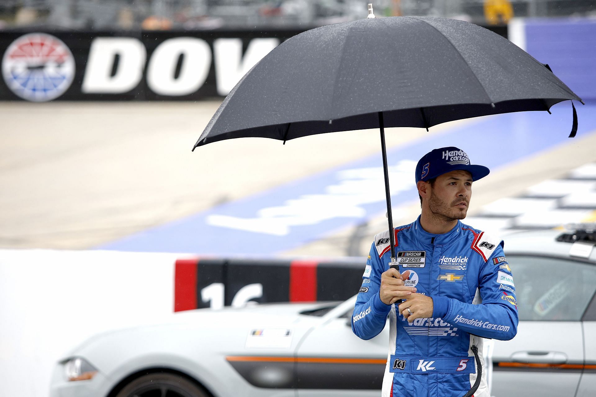 Kyle Larson looks on from under an umbrella during a rain delay in the NASCAR Cup Series DuraMAX Drydene 400 presented by RelaDyne at Dover Motor Speedway.
