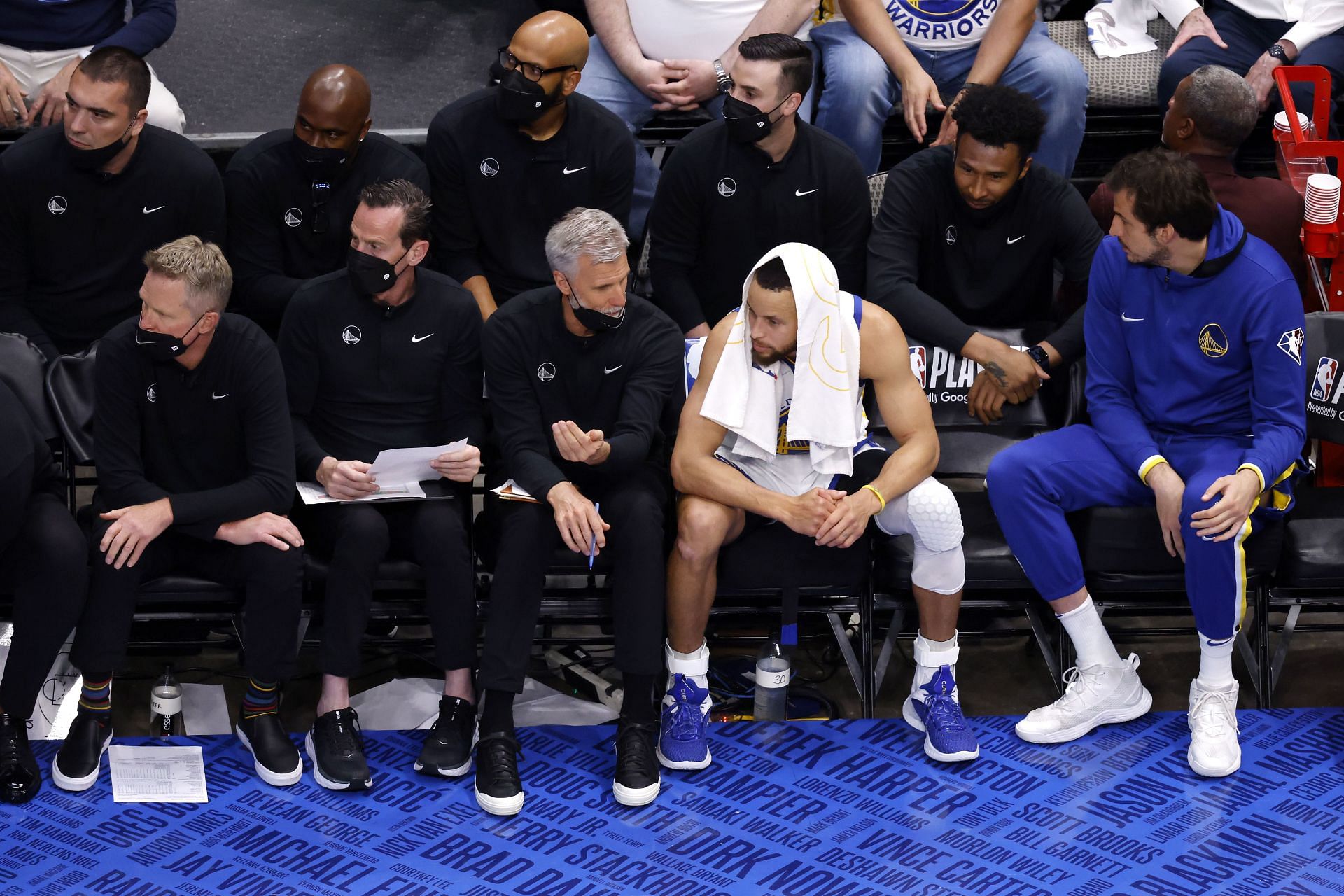Steph Curry of the Golden State Warriors looks on from the bench with his assistant coaches.