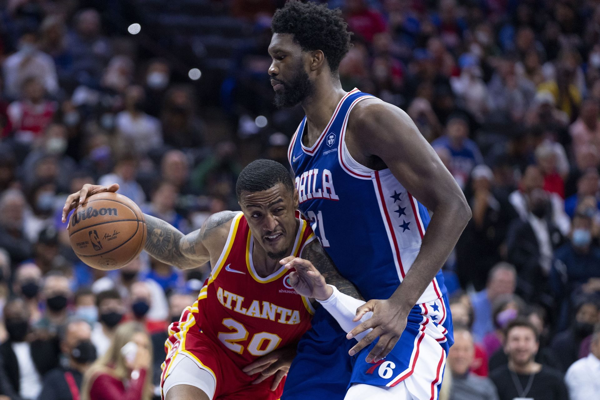 John Collins attempts to drive past Joel Embiid.