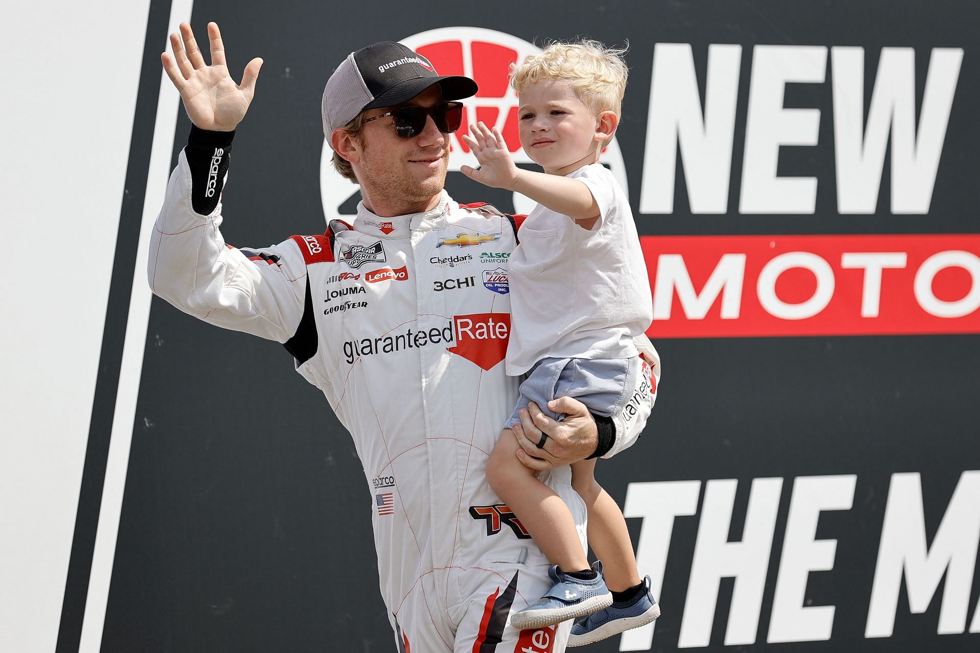 Tyler Reddick waves to fans as he walks onstage with his son, Beau during driver intros before the 2022 NASCAR Cup Series Ambetter 301 at New Hampshire Motor Speedway in Loudon, New Hampshire. (Photo by Tim Nwachukwu/Getty Images)