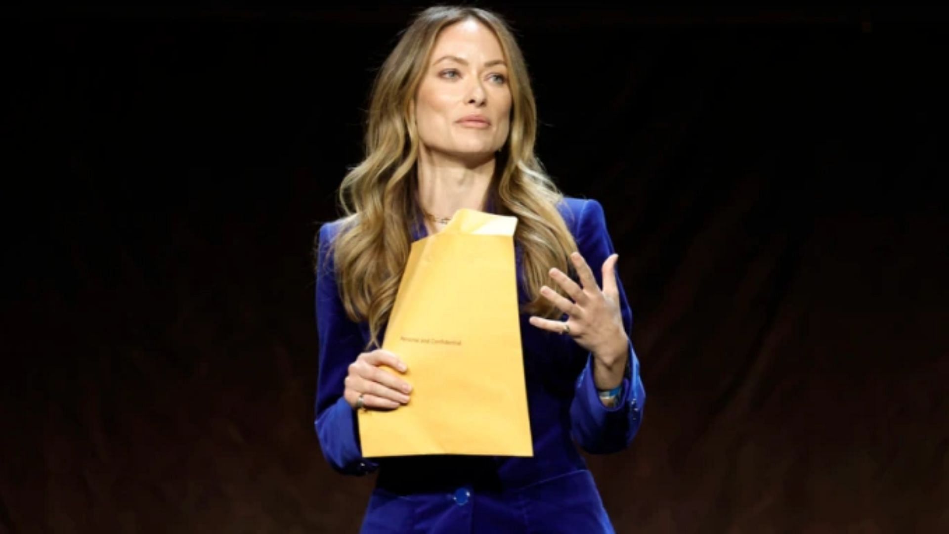 Olivia Wilde holding the legal papers during her Cinema Con presentation. (Image via Getty Images/Frazer Harrison)