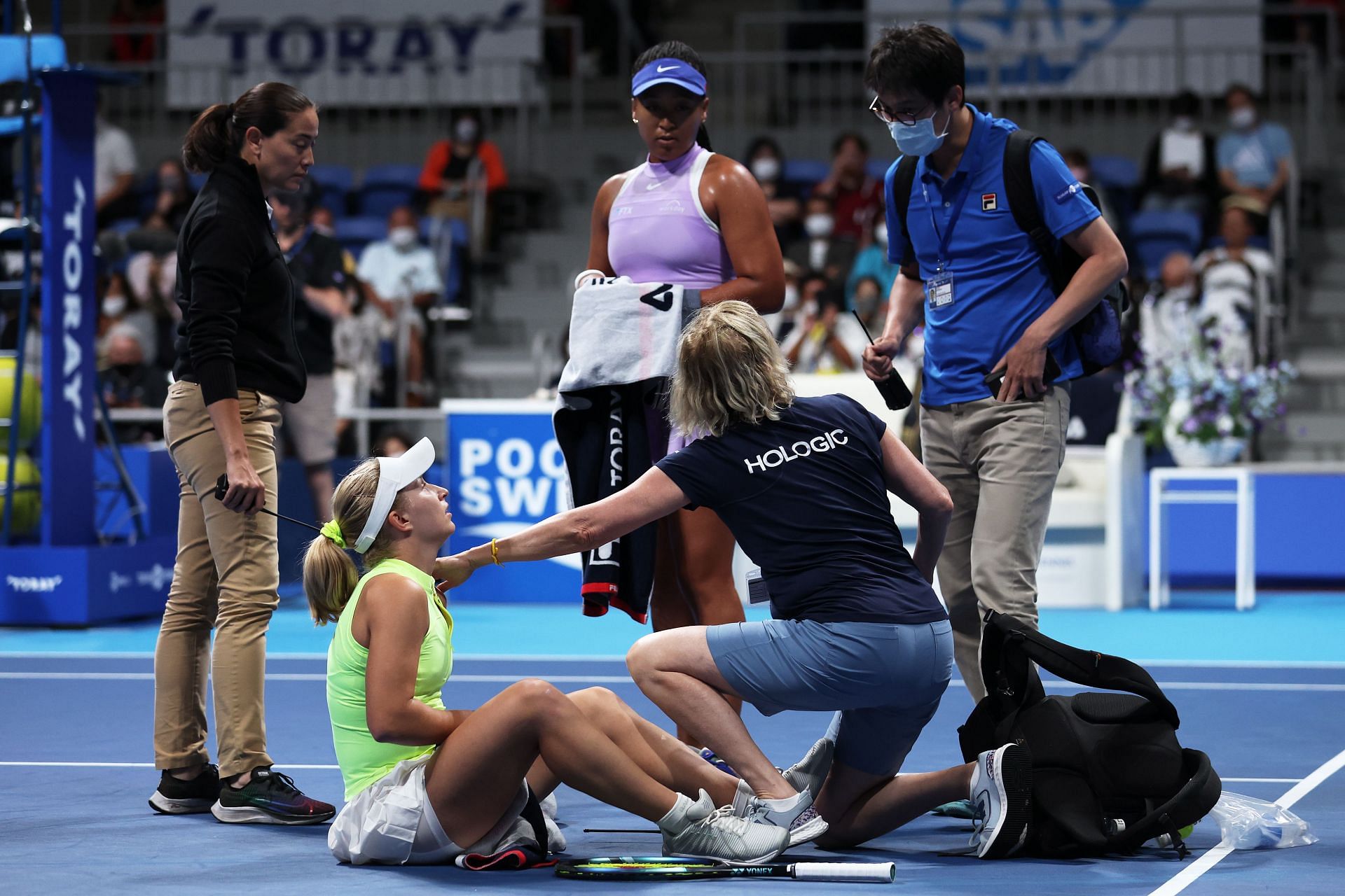 Daria Saville (bottom left) receives medical attention as Naomi Osaka looks on in Tokyo.