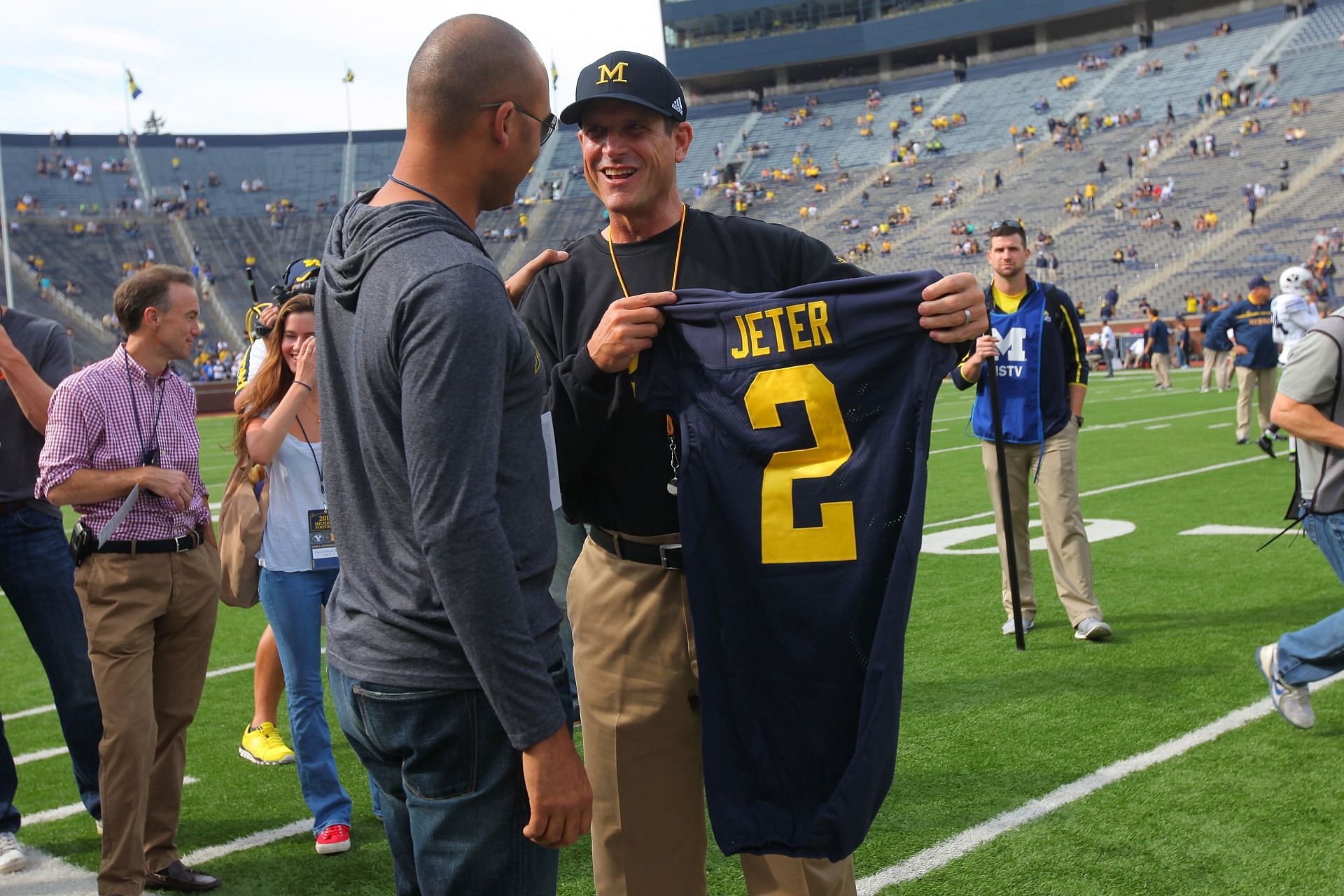 Jim Harbaugh of the Michigan Wolverines presents Derek Jeter (L) with a jersey at Michigan Stadium