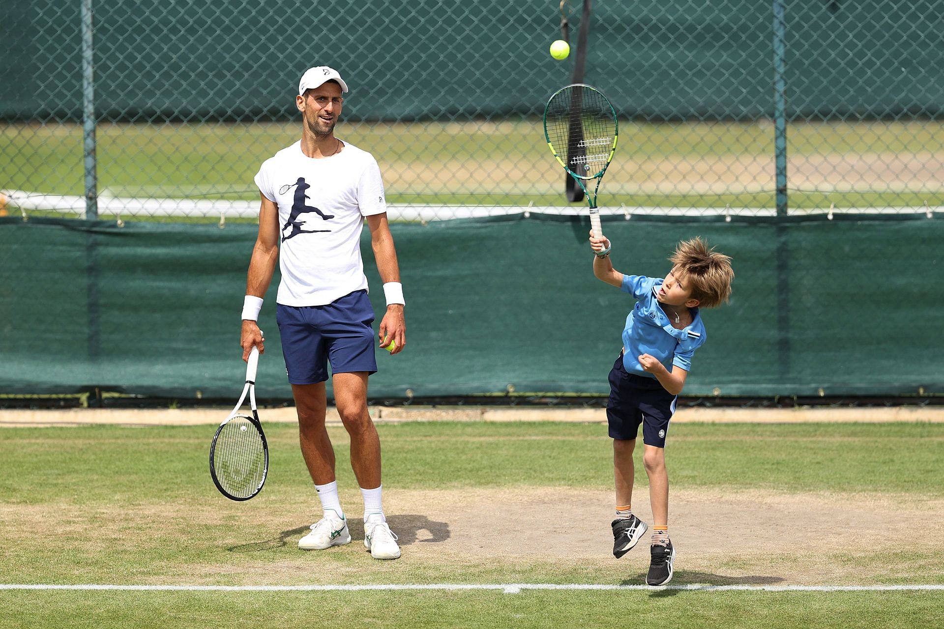 Novak Djokovic (left) looks on as son Stefan (right) serves in the practice courts of Wimbledon last July.