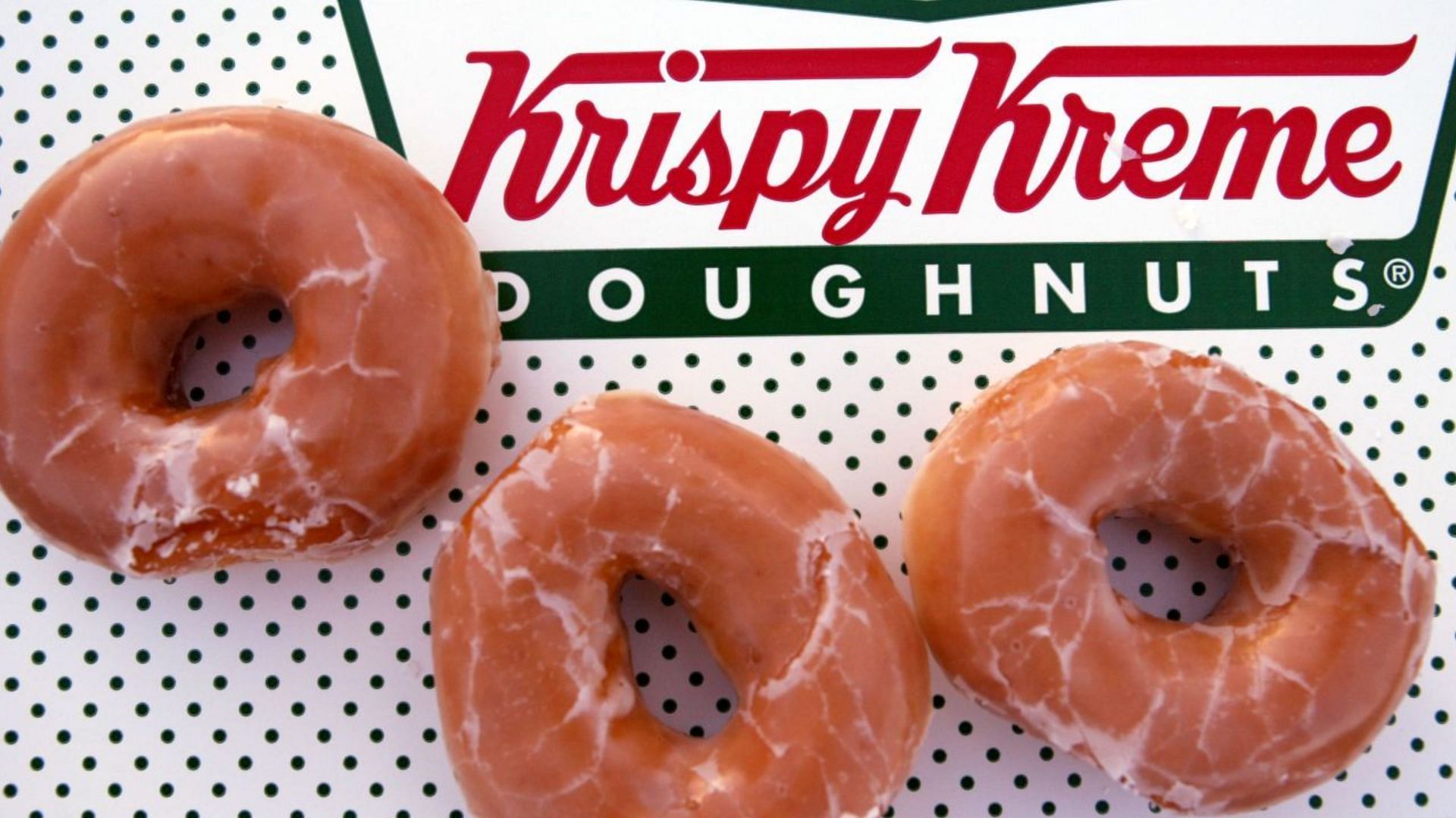 the Krispy Kreme logo with some glazed donuts (Image via Joe Raedle/GettyImages)