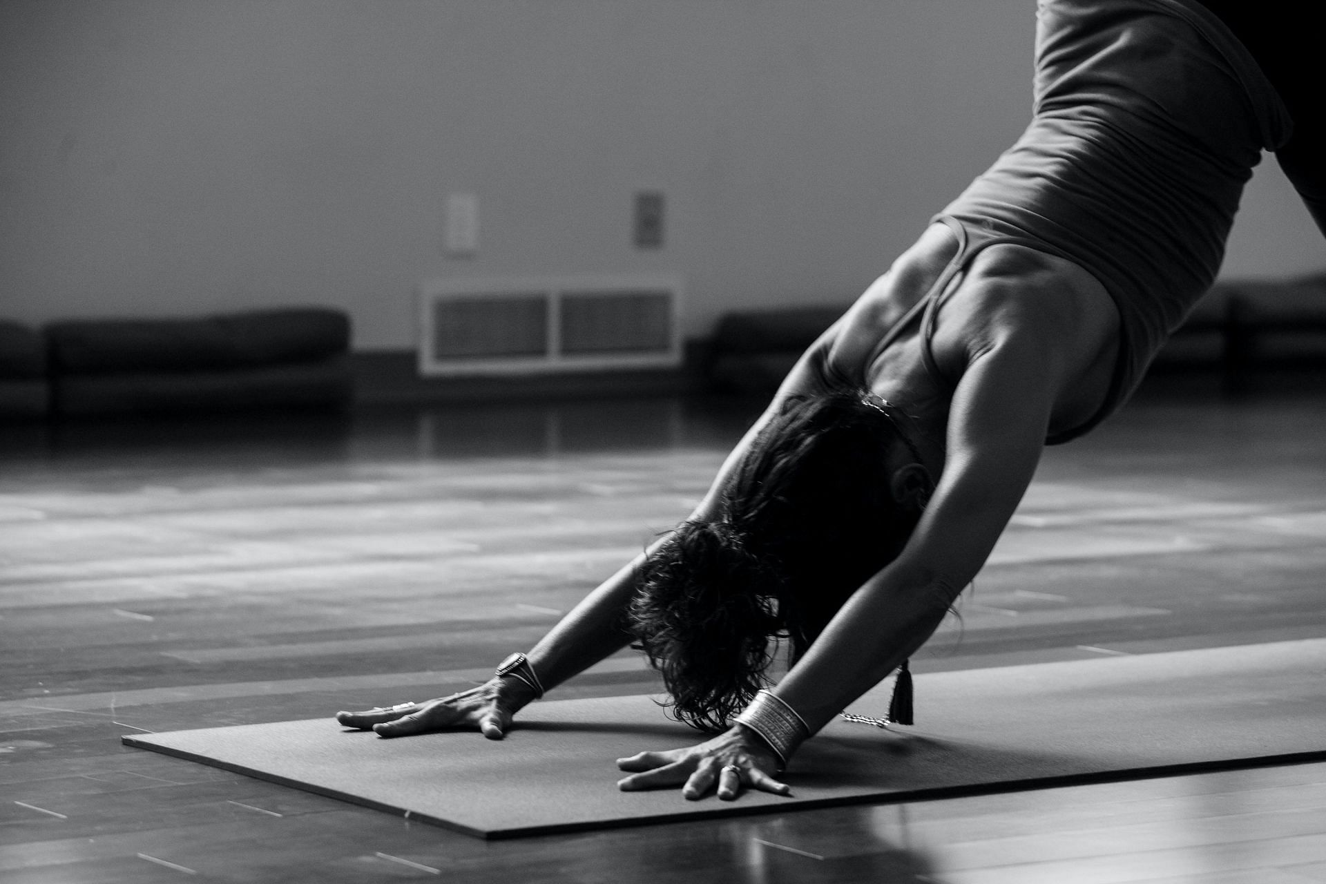 A black and white image of a woman performing a downward dog pose on a yoga mat.
