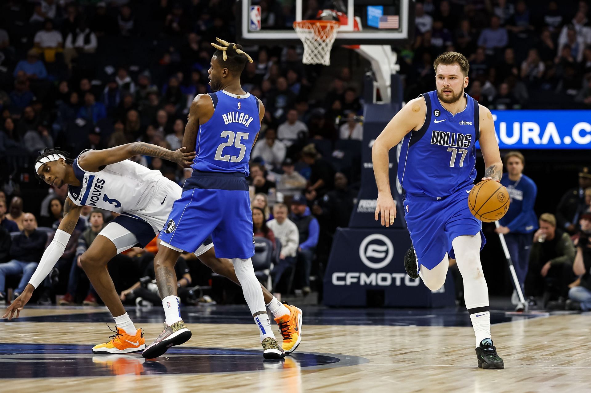 Luka Doncic of the Dallas Mavericks dribbles the ball upcourt as teammate Reggie Bullock screens Jaden McDaniels of the Minnesota Timberwolves