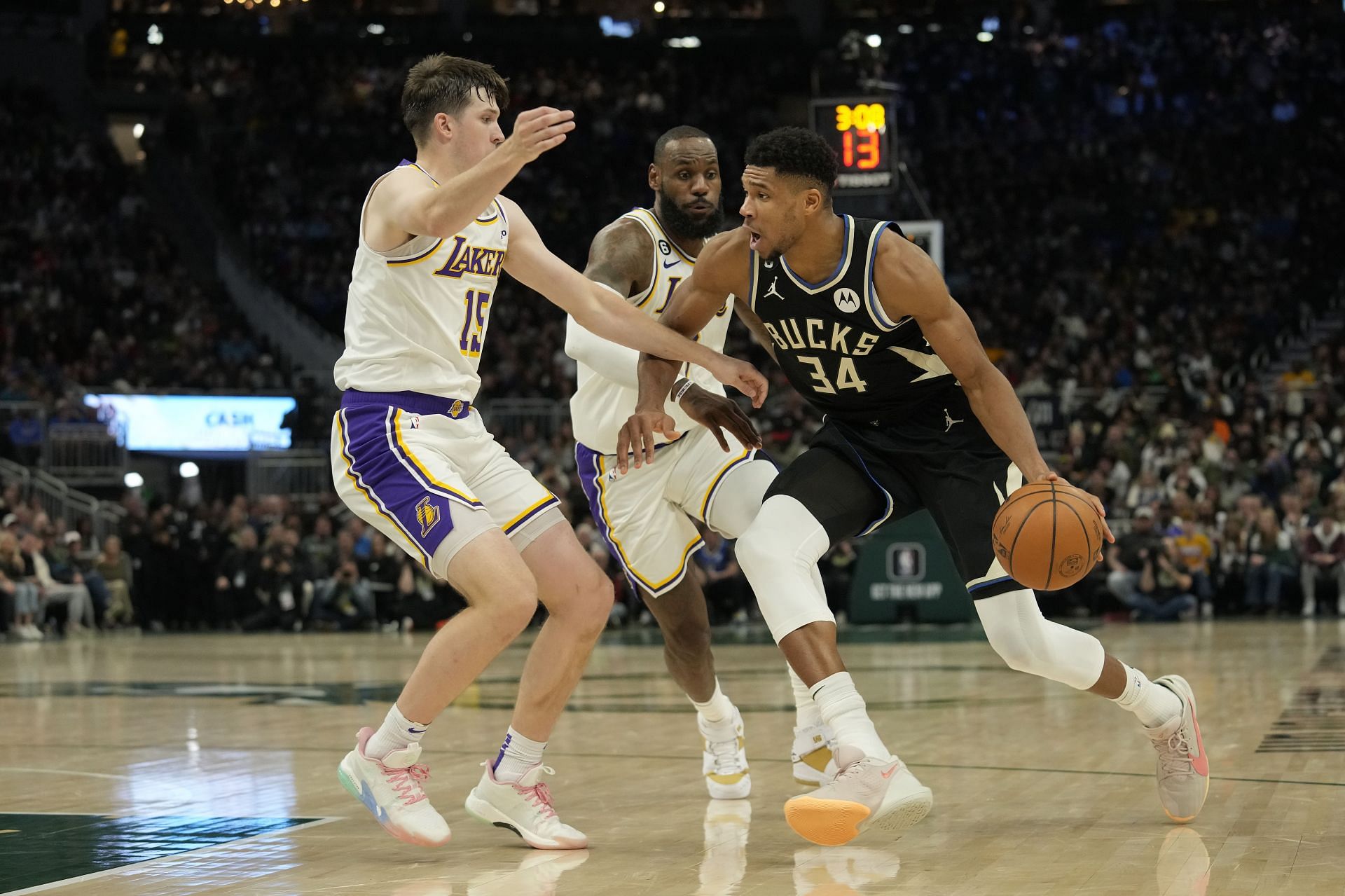 Giannis Antetokounmpo of the Milwaukee Bucks dribbles the ball against Austin Reaves and LeBron James of the Los Angeles Lakers.