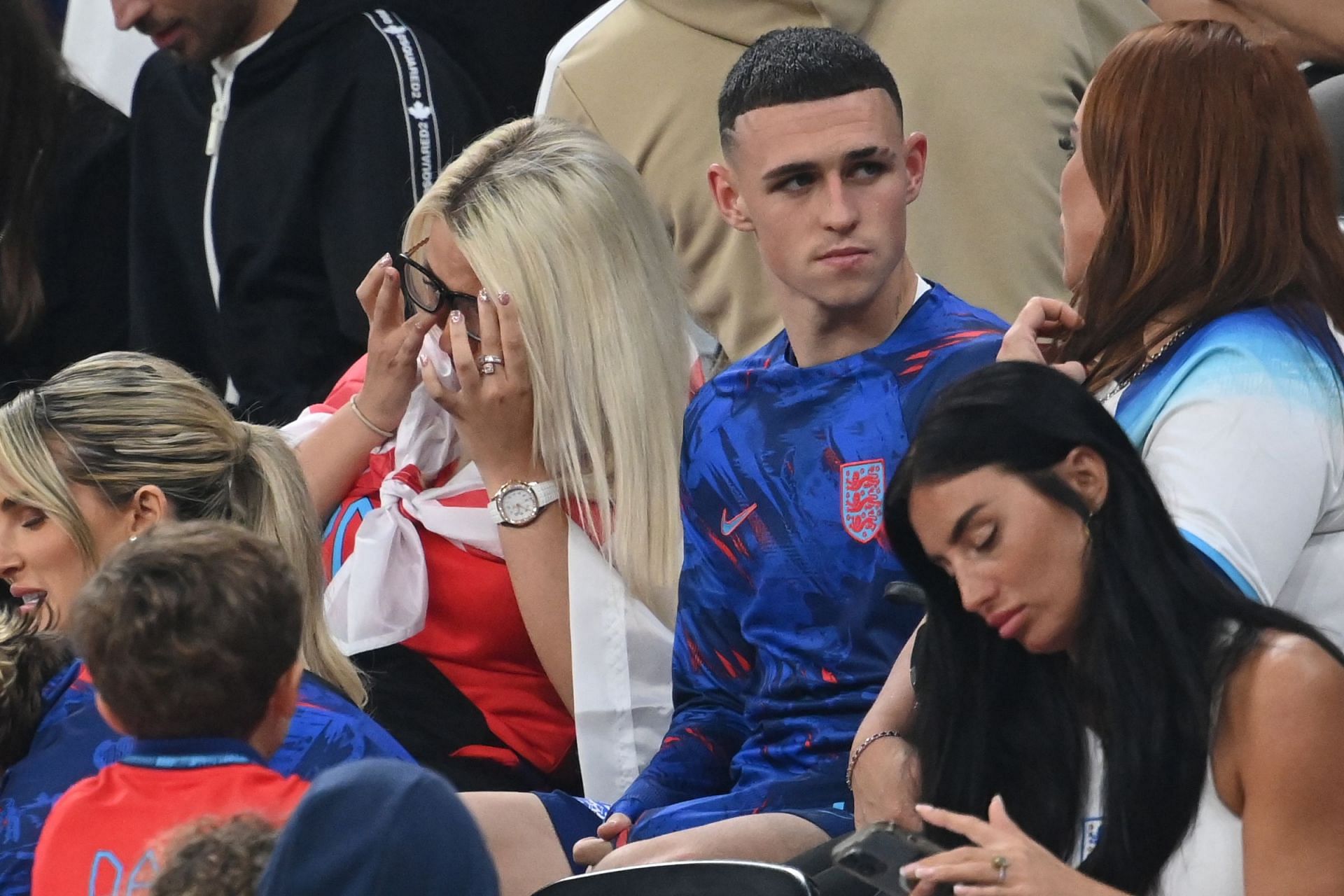 Phil Foden discusses with a family member while partner Rebecca Cooke wipes a tear. (Source WCNP via The Sun)