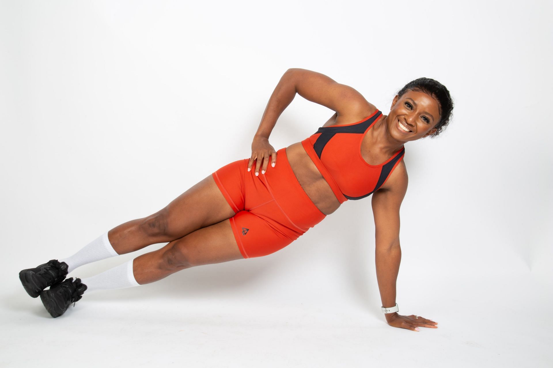 A woman performing the side plank, a popular core exercise, against a solid white backdrop.