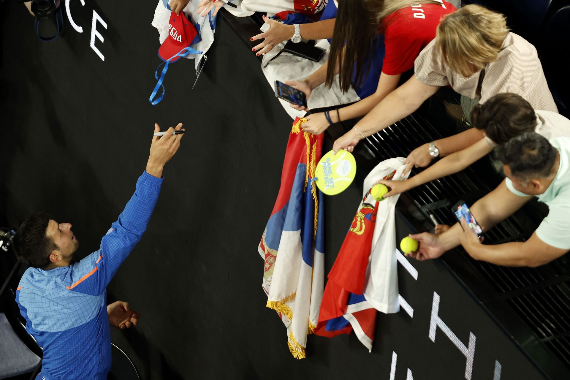 Novak Djokovic signs merchandise for spectators in the Semifinal singles match against Tommy Paul