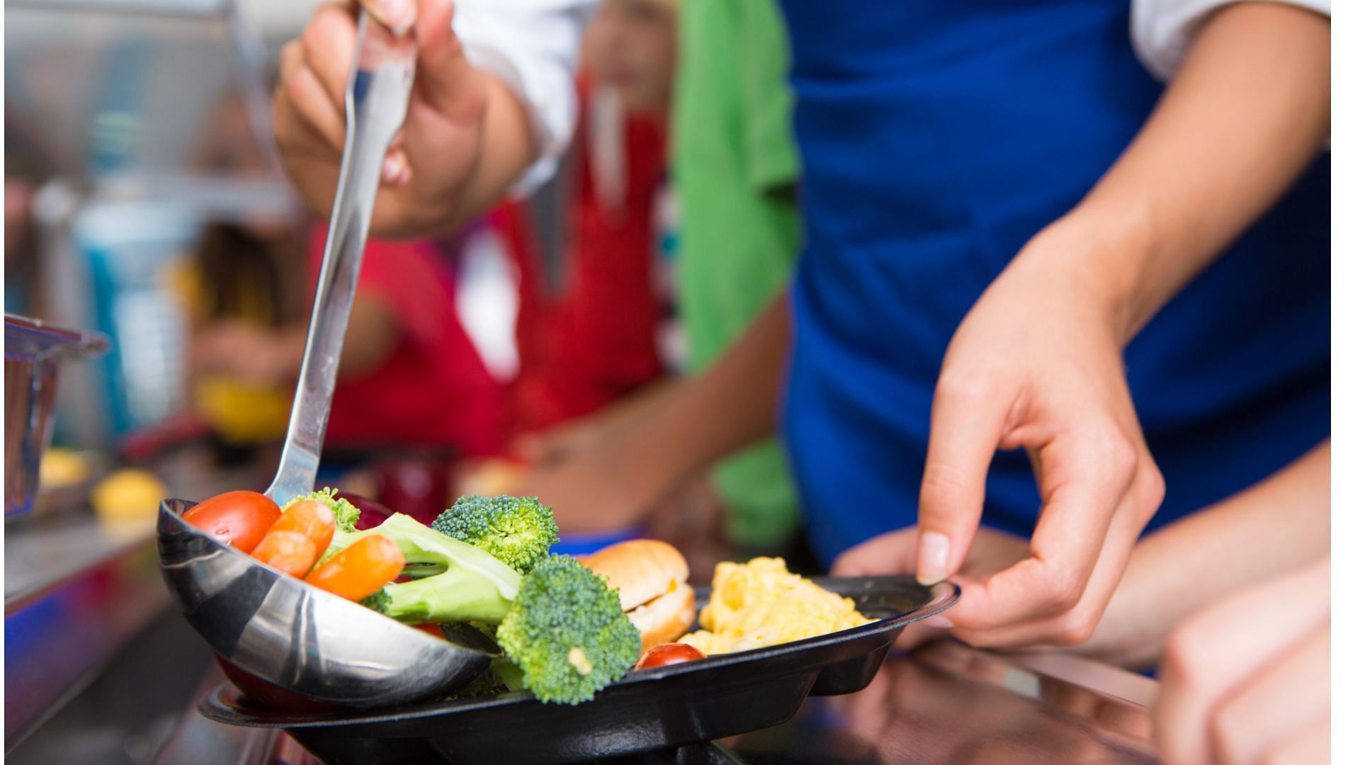 A staff member serves school meals to children on a tray (Image via SDI Productions/Getty Images)