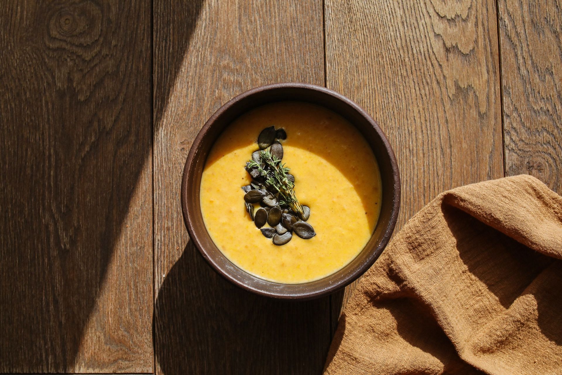 A bowl of roasted pumpkin seeds with a sprig of fresh thyme on a wooden table.