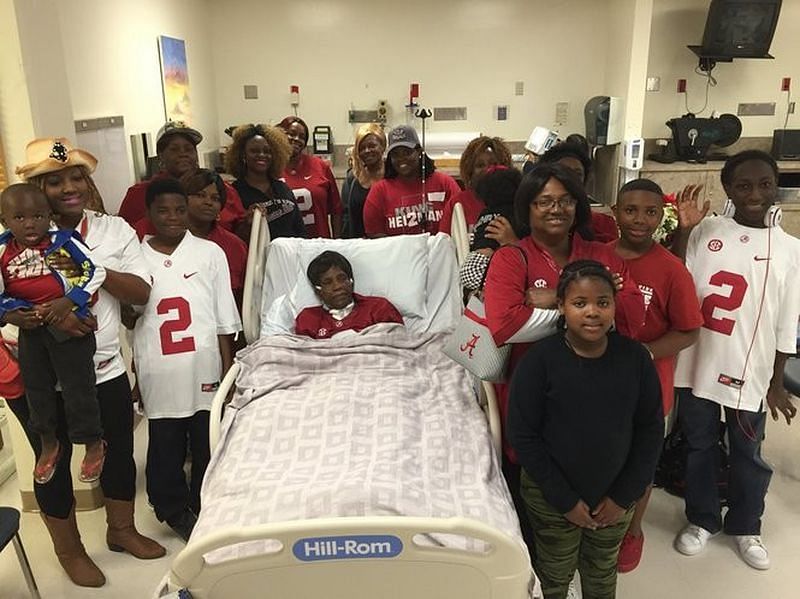 Gladys in her hospital bed surrounded by family during the Heisman ceremony. Photo via al.com