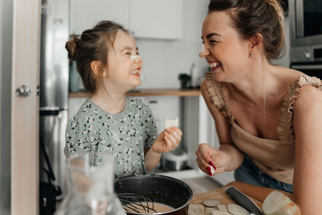 Playful mother and daughter preparing food together in kitchen