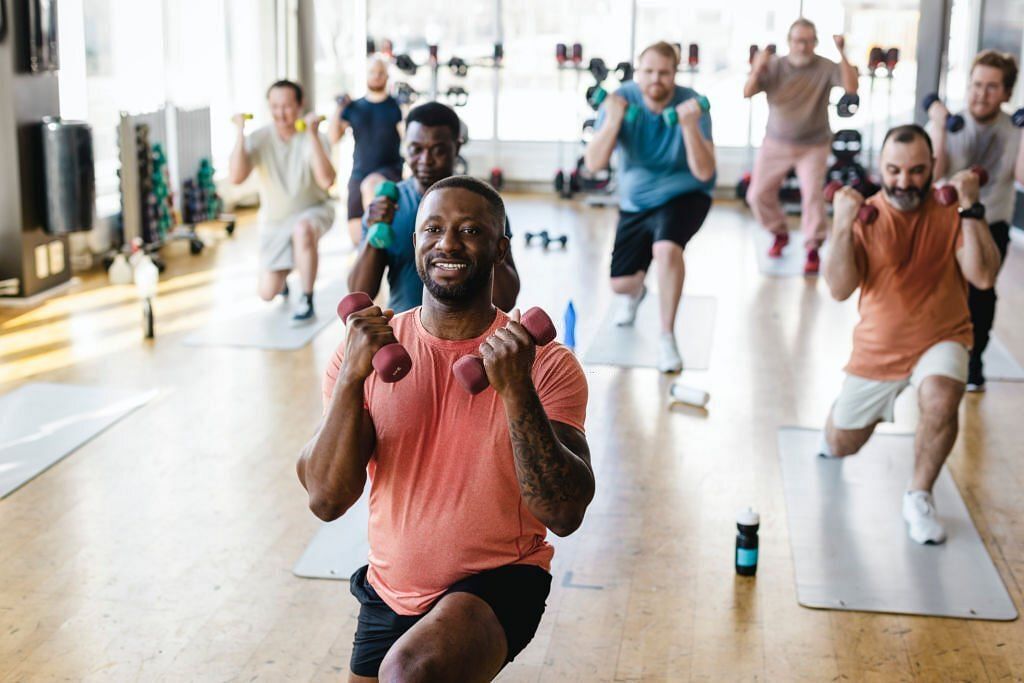 Smiling male fitness instructor practicing dumbbell exercise with men in gym 