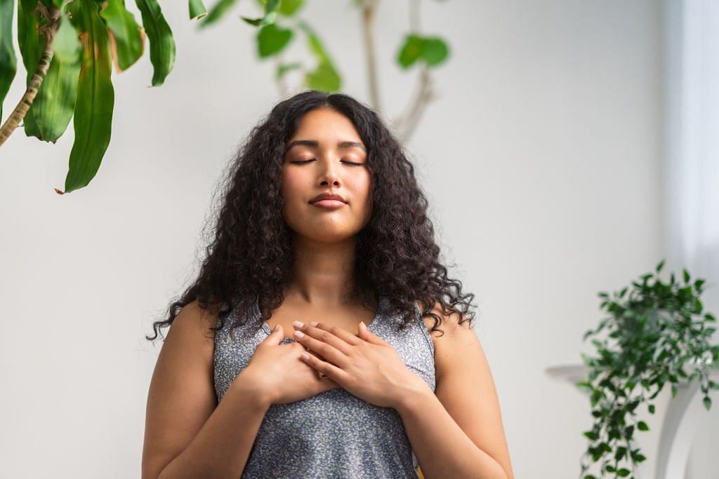 young multiracial woman is doing breathing exercise at home.