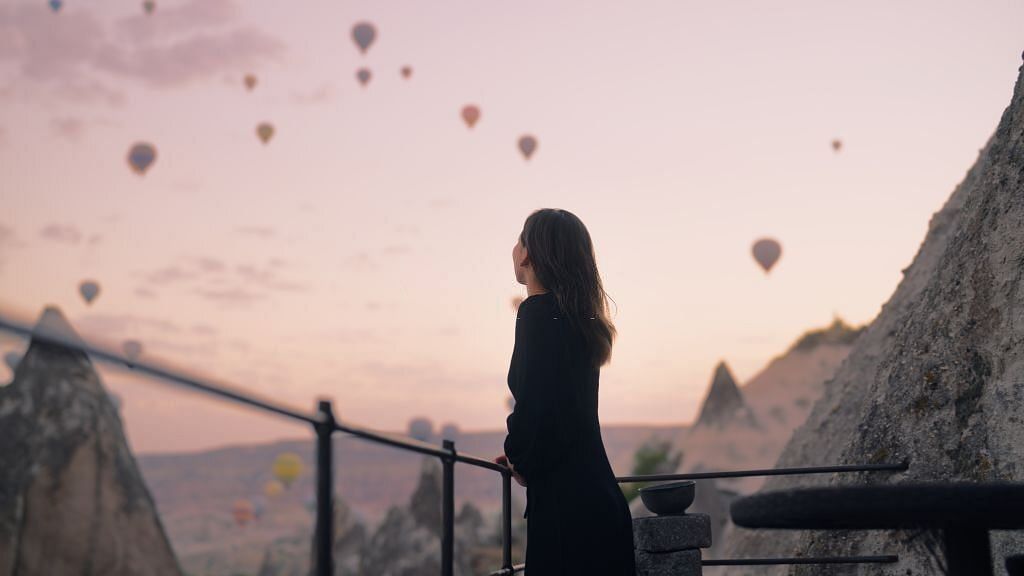A female tourist is enjoying watching hot air balloons flying in the sky at the rooftop of the hotel where she is staying during her vacation