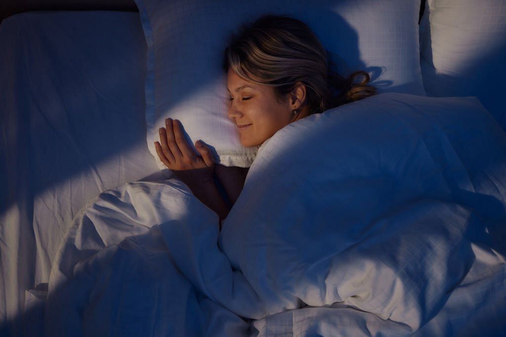 High angle view of young woman smiling while dreaming in bed at night
