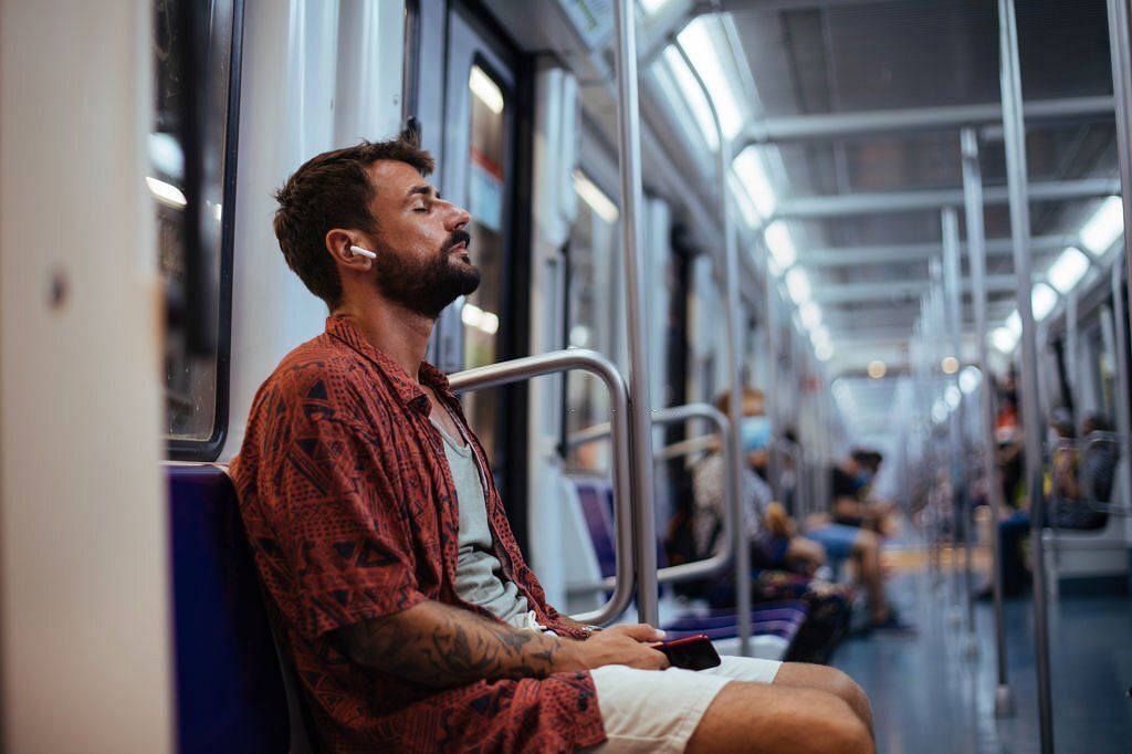 Young man listening to music on his headphones and resting while sitting on a subway train (Image via Getty Images)